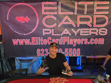 Smiling man holding poker trophies in front of Elite Card Players banner.