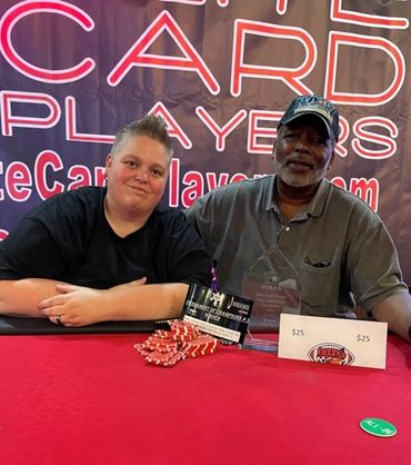 Two people posing at a poker event with chips and prize envelopes.