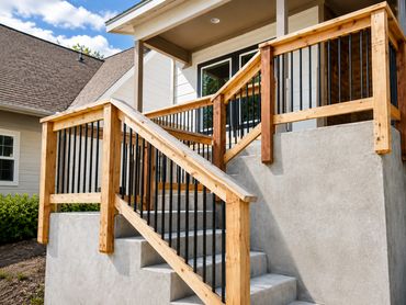 Concrete stairs with wooden and black metal railings leading to a porch.