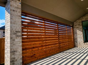 Sunlit wooden slatted wall casting striped shadows on patio floor.