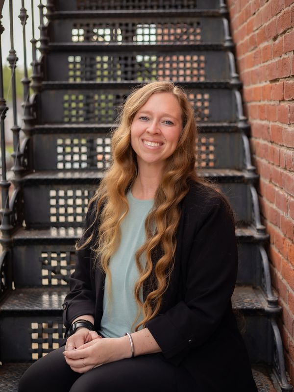 Woman with long hair smiling on metal stairs.