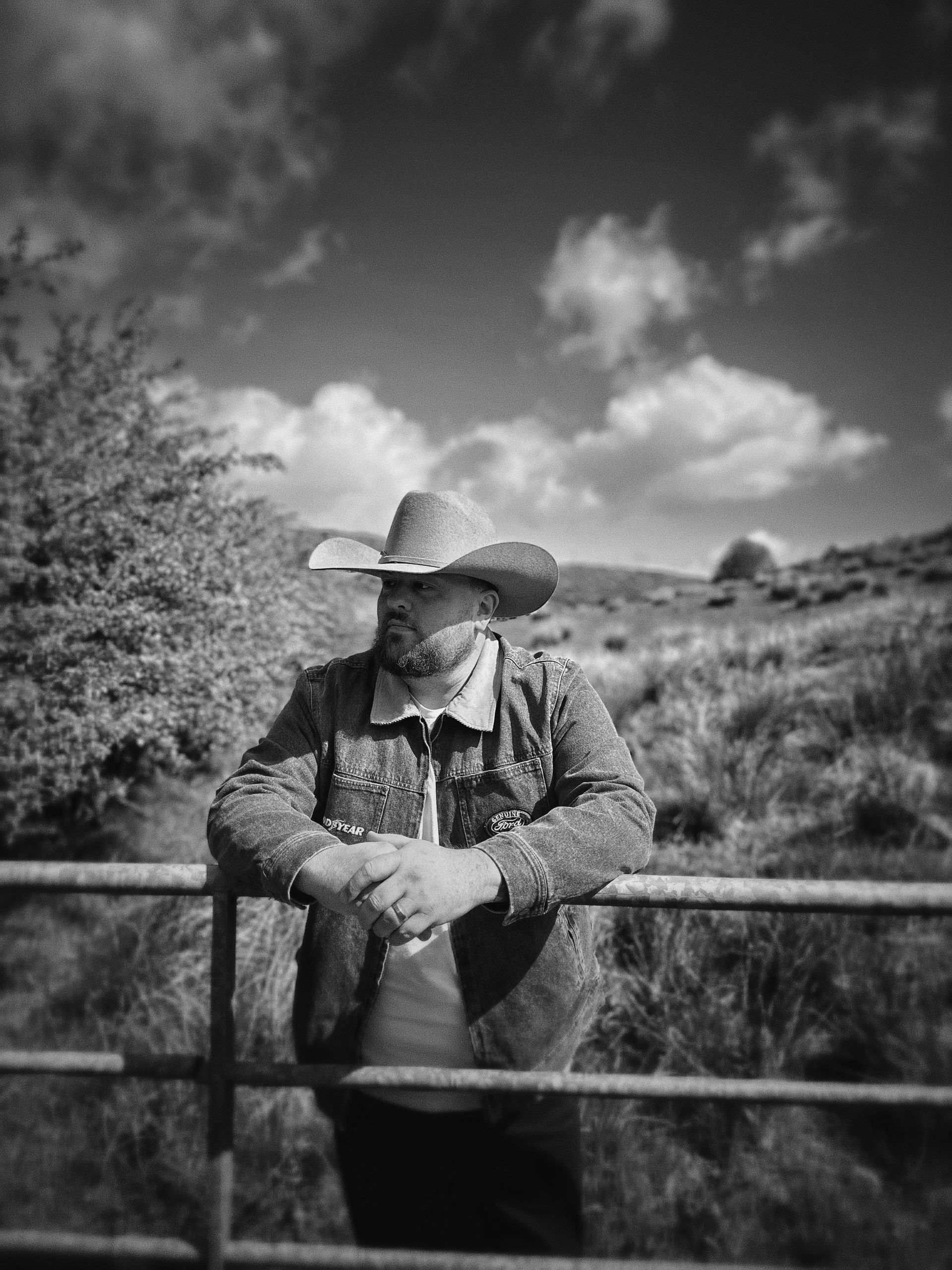 Man in cowboy hat leaning on a fence in black and white