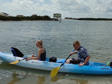 Two people kayaking while a third person stands in the water nearby.