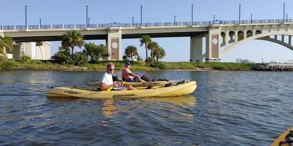 Two men kayaking near a bridge on a sunny day.