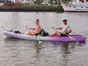 Two people kayaking on calm water near a dock with boats.