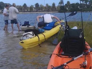 Two kayaks on the water with fishing gear and people preparing nearby.