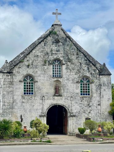 Front view of an old stone church with stained glass windows and cross on top.