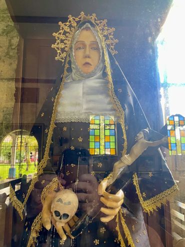 Religious statue holding a crucifix and skull, adorned in black and gold attire.