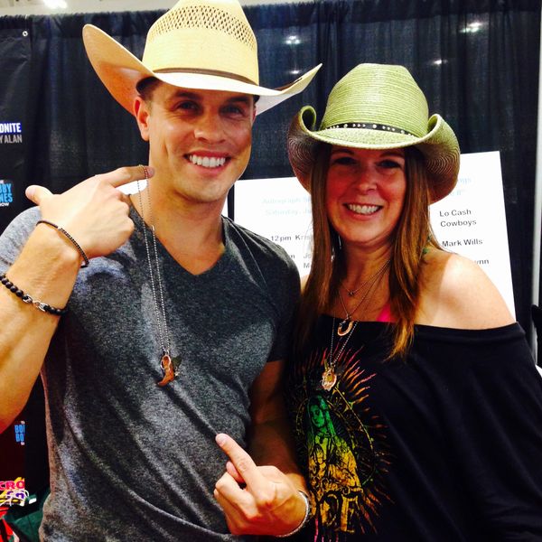 Two people wearing cowboy hats smiling and pointing at each other.