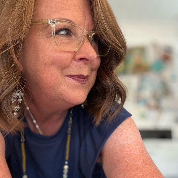 Smiling woman with glasses and jewelry in a casual setting.