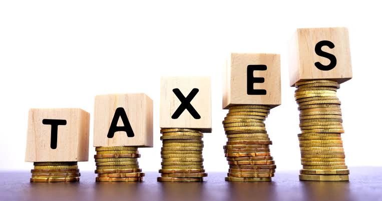 Wooden blocks spell TAXES on stacks of coins.