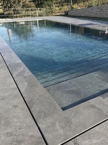 A serene outdoor swimming pool with clear water and stone tiles.