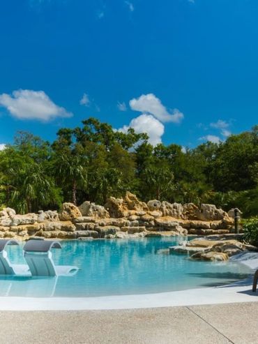 Tropical pool area with lounge chairs and lush greenery under blue sky.