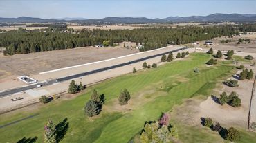 Aerial view of a golf course next to a long paved track in a rural area.