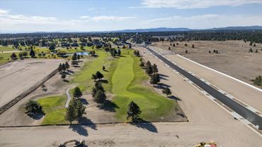 A golf course beside a newly paved road under construction in a semi-rural area.