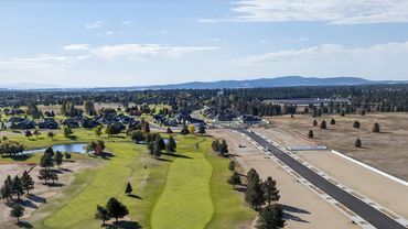 A golf course beside a newly paved road under construction in a semi-rural area.