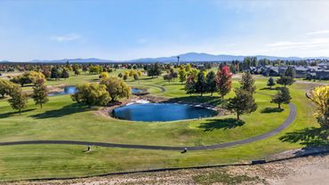 A scenic golf course with ponds, trees, and mountains under a clear blue sky.