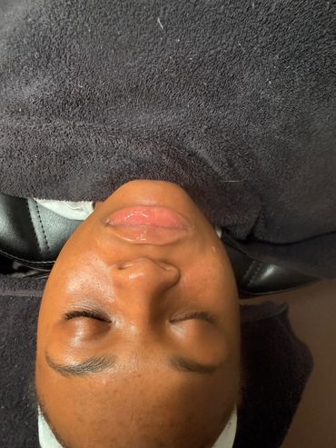 Person resting with eyes closed under a black towel on a chair.