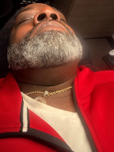 Close-up of a man with a gray beard wearing a gold chain and red jacket.