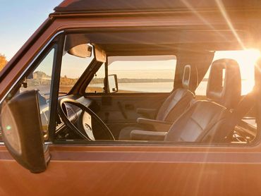 Sunlit interior of a vintage car by the water at sunset.