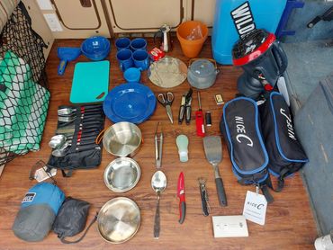 Organized camping kitchen tools and utensils neatly laid out on a wooden floor.