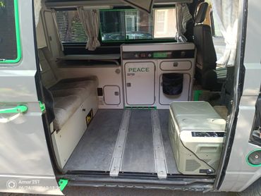 Interior of a camper van with seating, kitchenette, and cooler.