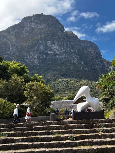 Tourists walk near a large white sculpture with a mountain backdrop.