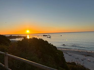 Sunset over a peaceful beach with boats and people relaxing.