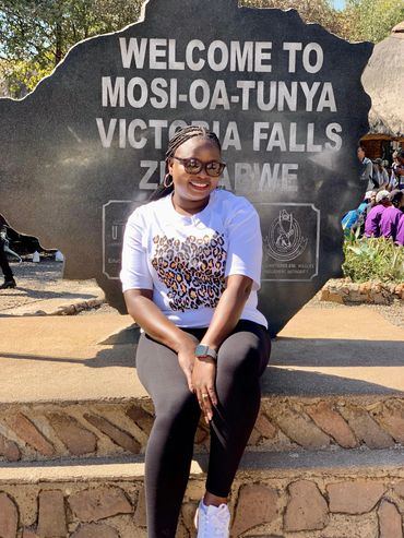 Smiling woman posing in front of Victoria Falls welcome sign in Zimbabwe.