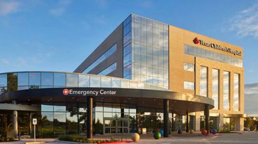 Modern hospital emergency center with glass facade under a clear sky.