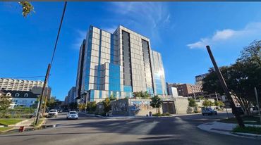 Modern glass high-rise building under clear blue sky at street intersection.