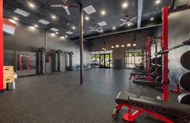 Spacious gym with black and red workout equipment and rubber flooring.