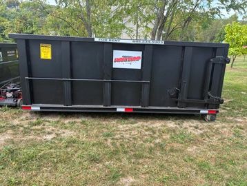 Large black rental dumpster on grass with contact information visible.