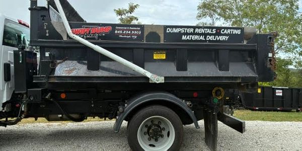 A black dumpster rental truck with signage for Swift Dump services.