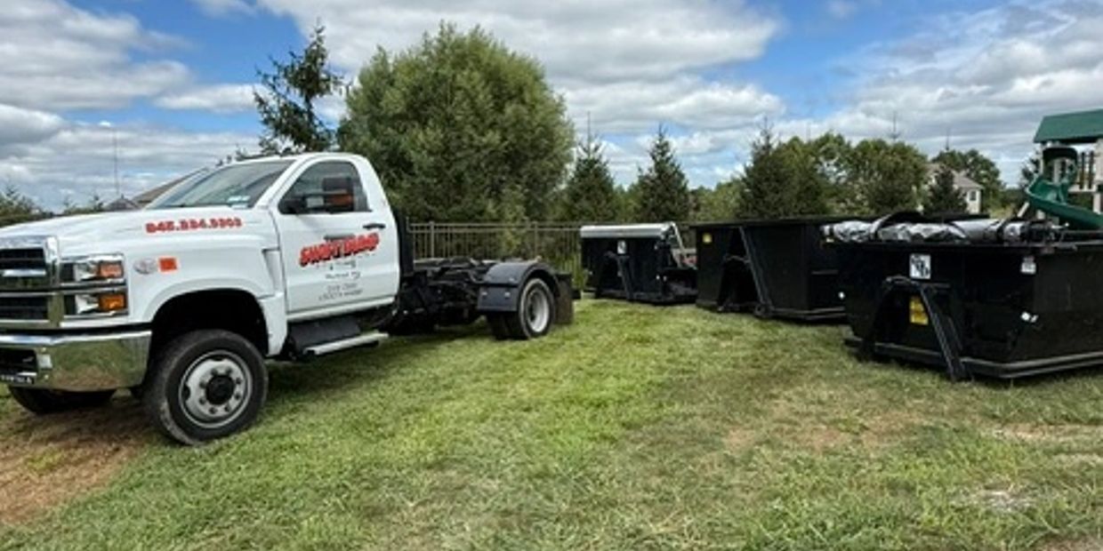 White truck parked on grass with black dumpsters nearby under a cloudy sky.