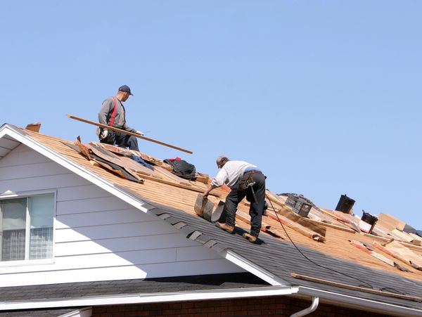 Two workers installing new shingles on a residential roof under clear blue sky.