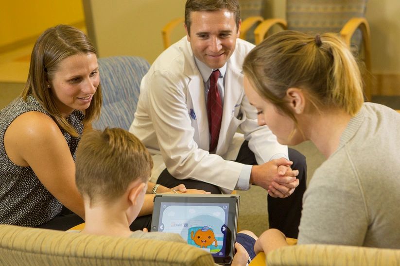 Image of a child holding a tablet with a doctor, child life specialist and designer