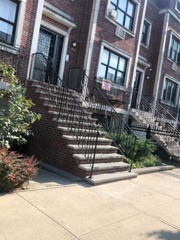 Brick townhouse with decorative black iron railings and front steps.