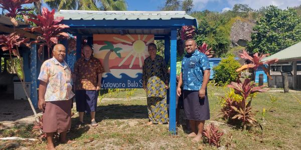 Four people posing near a colorful sign under a shelter.