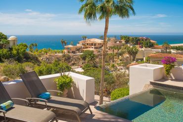 Ocean view from a serene patio with lounge chairs and a pool.