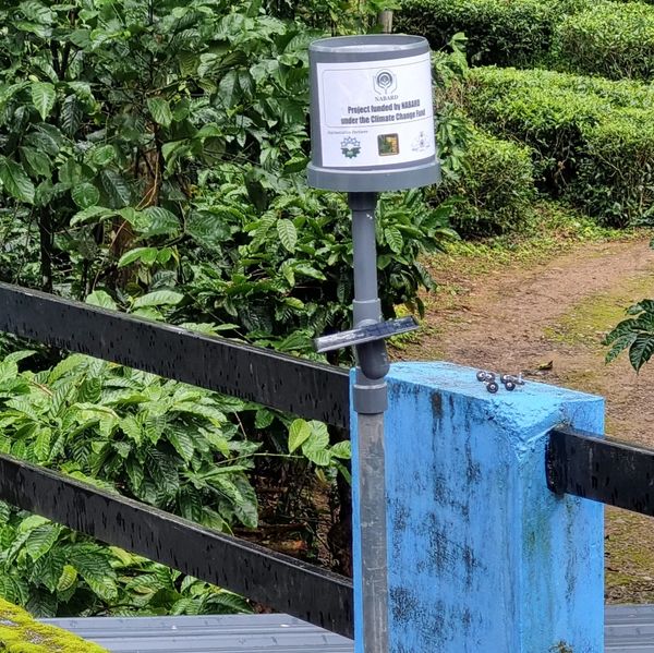 A device labeled as a climate change project sits near a blue-painted post and greenery.