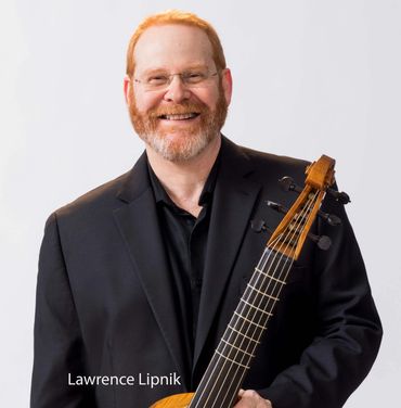 Smiling man with red hair and beard holding a stringed instrument.