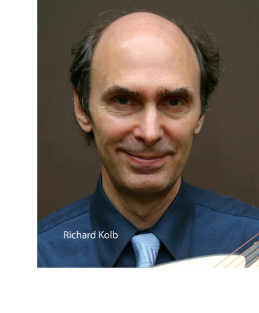 Portrait of a smiling man in a blue shirt and tie holding a guitar.