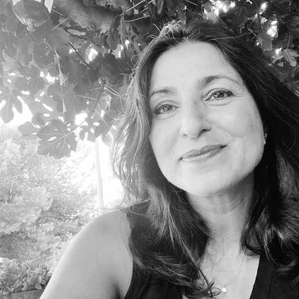 Black and white close-up of a smiling woman outdoors under leafy branches.