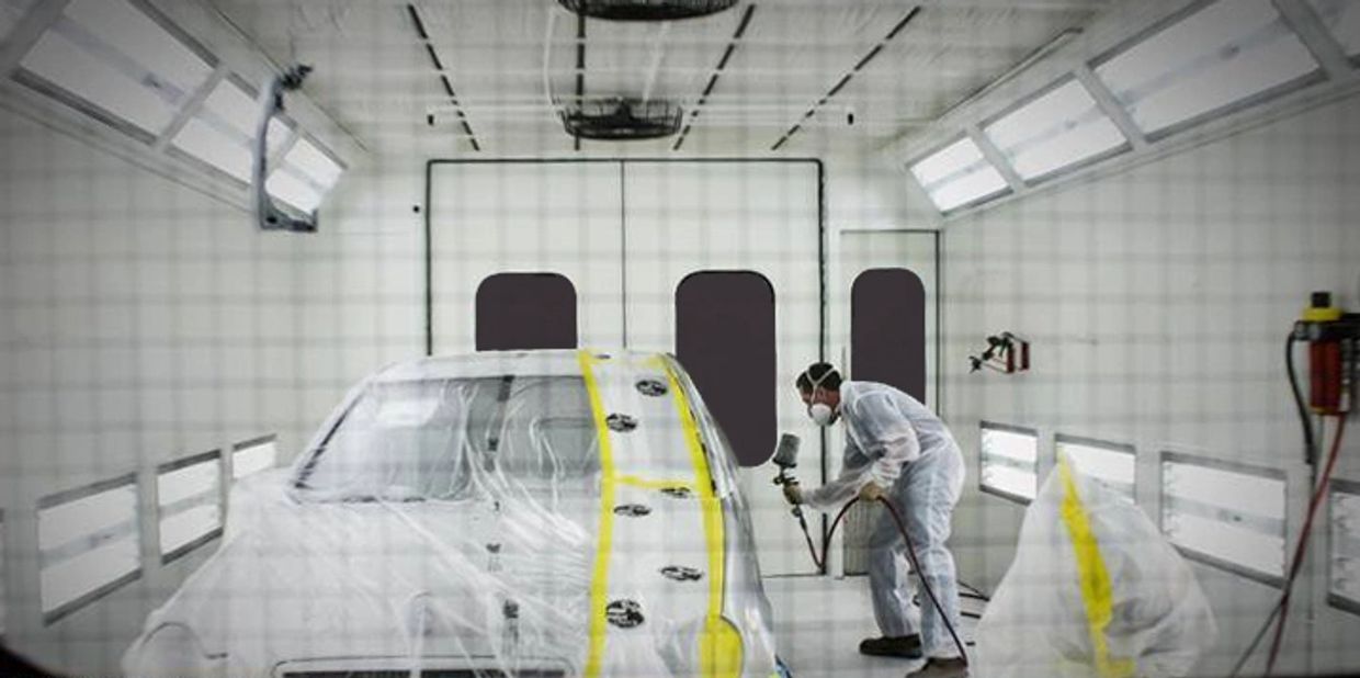 A technician in a auto body shop cabin, painting a white car.
