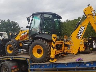 A yellow JCB backhoe loader on a flatbed truck.