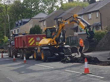 Construction workers using a JCB excavator to break up asphalt on a residential street.
