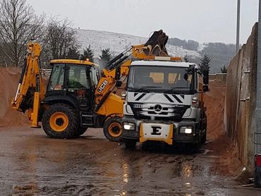 A yellow JCB loader and a white Mercedes truck on a muddy construction site.