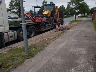Construction vehicles loaded on a flatbed truck by the roadside.