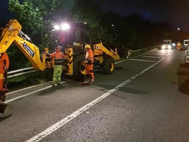 Nighttime road construction with workers and machinery under streetlights.